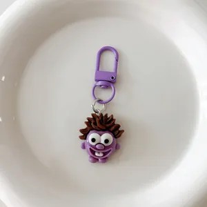 Close-up detail of funny cartoon monster keychain pendant with purple clasp and messy hair.