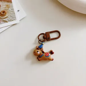 Detail shot of a cute brown running pony keychain with a blue party hat and metal lobster clasp.