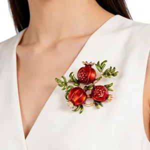 Detailaufnahme der eleganten Granatapfel-Brosche mit rotem Emaille und grünen Blättern.