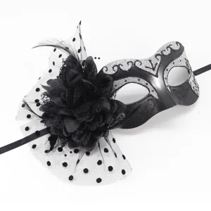 Black masquerade mask detail featuring tulle mesh, large flower, and glittering silver scroll pattern.