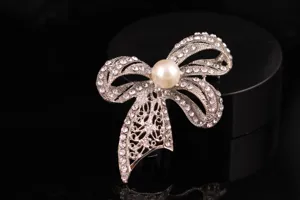 Primo piano di una spilla con fiocco in strass luminosi e perla centrale con finitura argento.