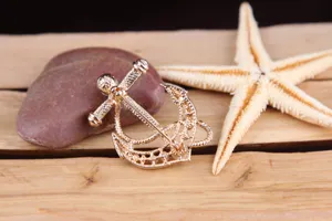 Golden anchor brooch detail showcasing elegant pearl and sparkling rhinestone embellishments.