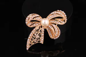 Primo piano dettagliato della spilla con fiocco in strass dorato e perla artificiale centrale.