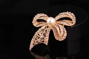 Squisita spilla a fiocco dorata con strass scintillanti e perla centrale per le donne.