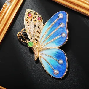 Gros plan sur les détails de la broche papillon avec filigrane doré et émail dégradé bleu.