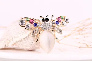 Close-up detail shot of a sparkling rhinestone and cat's-eye stone bee brooch on a shell prop.