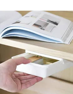 Detalle de cajón adhesivo bajo escritorio con almacenamiento fluido para pequeños artículos.