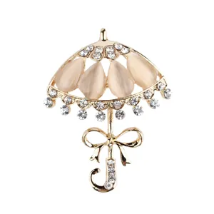 Elegante spilla a forma di ombrello dorata con brillanti strass e pietre occhi di gatto.
