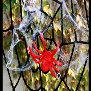 Close-up detail shot of Halloween red plush spider decoration with fake white spider web props.