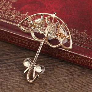 Gold umbrella brooch detail, alloy accessory with white inlay on vintage book prop.