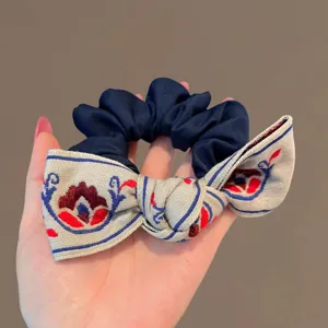 Détail en gros plan d'un chouchou pour cheveux bleu marine avec un nœud brodé élégant.