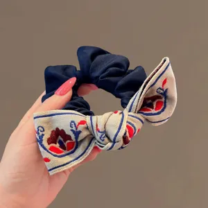 Gros plan détaillé d'un chouchou bleu foncé avec un nœud brodé beige pour coiffure.