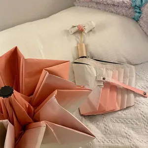 Détail d'un magnifique parapluie pliant à dégradé rose pastel posé sur un lit blanc.
