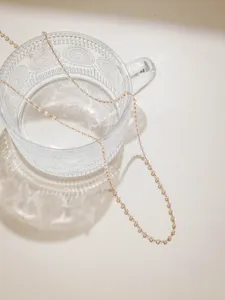 Close-up detail of delicate pink crystal bead stainless steel chain draped on a clear glass cup.