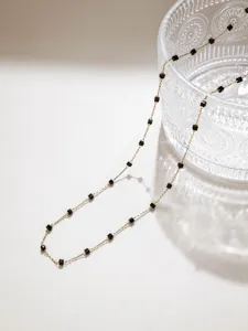 Vista dettagliata della collana con catena dorata delicata e perline cubiche nere.