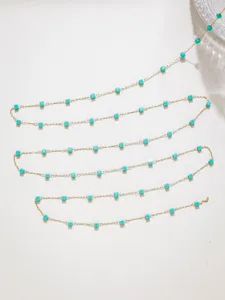 Primo piano di sottile catena in acciaio dorato con perline quadrate turchesi per gioielli DIY.