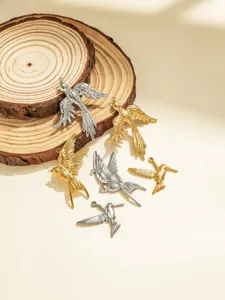Closeup of stainless steel bird pendants on wood slice, detailed jewelry crafting accessories.