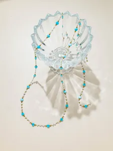 Gros plan détaillé d'une chaîne de perles turquoise et dorées délicate dans bol en verre.