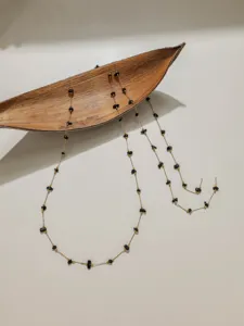 Close-up detail of delicate stainless steel chain with black stone chips and gold beads.