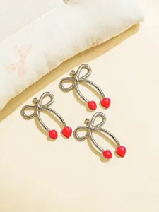 Detail shot of three silver bow and red heart cherry metal pendants for DIY jewelry crafting.