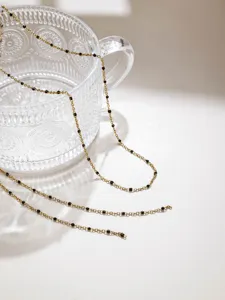 Detail shot of gold fine chain with black beads on glass cup, ideal for DIY doll clothes.
