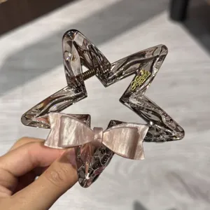 Dettaglio ravvicinato della molletta per capelli a stella in acetato con fiocco rosa lucido.