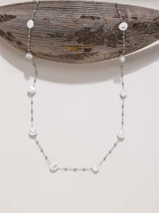 Close up detail view of long silver plated chain necklace decorated with natural baroque pearl elements.