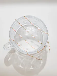 Close-up detail of pink shell rice beads on golden chain for handmade jewelry design.