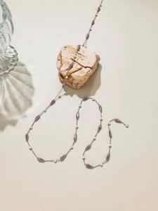 Close-up detail of DIY beaded jewelry chain with purple teardrop beads and pearls on stone.
