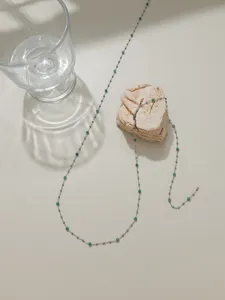 Detail shot of delicate stainless steel chain with small green crystal beads for DIY jewelry.