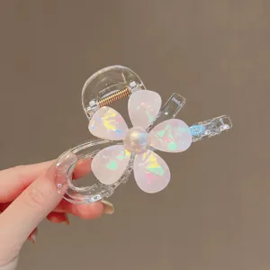 Nahaufnahme der transparenten Haarklammer mit schillernder Blume und Perle in Hand.