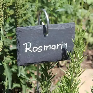 Natural slate plant marker detail with metal hook and white Rosmarin text in garden background.