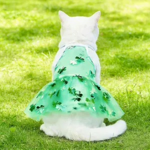 Detail shot of a cute white cat wearing a green sheer clover pattern pet dress on grass.