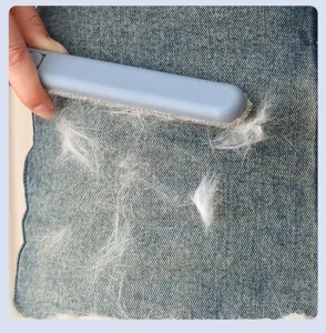 Detail shot of the long handle double sided hair removal brush cleaning pet hair on denim fabric.