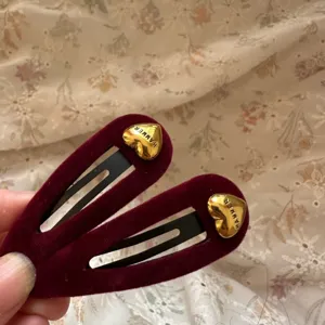 Vista detallada de pinzas para el cabello de terciopelo rojo oscuro con dijes de corazones dorados.