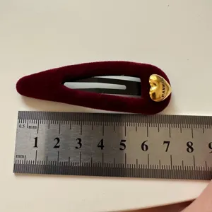 Detalle de pinza de pelo de terciopelo burdeos con corazón dorado y regla metálica de medida.