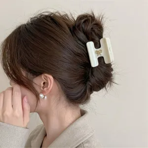 Primo piano dettagliato di un elegante fermacapelli bianco a forma di H con fiocco dorato.