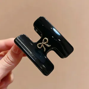 Primo piano dettagliato del elegante fermaglio per capelli nero a H con fiocco dorato.