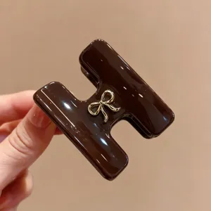 Primo piano del morsetto per capelli in acetato marrone a forma di H con fiocco dorato.