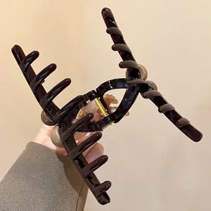 Nahaufnahme einer großen braunen Haarklammer aus Harz mit Perlendekor und starker Metallfeder.