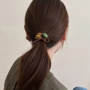 Vue détaillée d'un élastique à cheveux mignon ours brun avec perle verte sur queue de cheval.