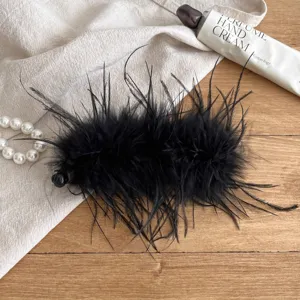Detailed close-up of a black fluffy feather banana clip hair accessory on linen fabric.