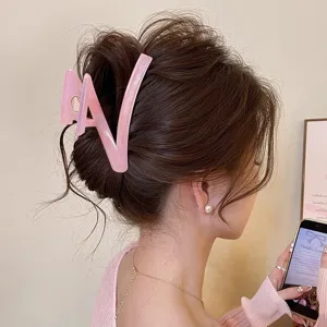 Détail de pince à cheveux lettre pailletée rose, accessoire élégant pour coiffure chignon.