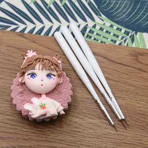 Fine detail paint brushes with white handles and cute clay doll head ornament for DIY art.