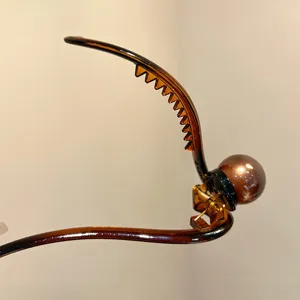 Close-up detail of the elegant brown tortoiseshell hair claw clip featuring a glossy pearl ball accent.