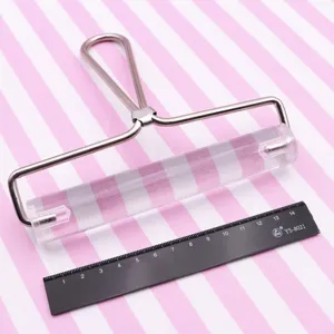 Detalle del rodillo de acrílico para arcilla, cilindro transparente con mango sobre fondo rosa.