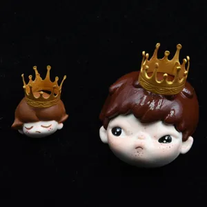 Closeup of cute cartoon doll head resin charms with gold crown for DIY crafts and decor.