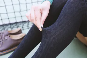 Detailed view of women's black cable-knit over-the-knee socks, showing stretch and texture.