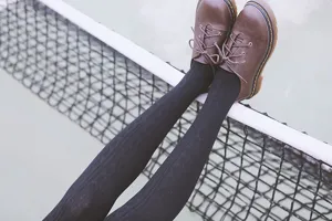Detail shot of black cable knit over-the-knee socks paired with brown shoes on court.