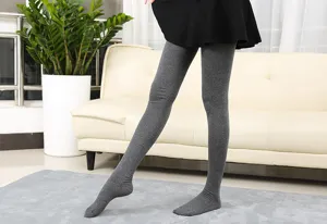 Detail view of grey over-the-knee long socks worn with black skirt in indoor room setting.